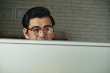 Asian entrepreneuir in glasses reading information on computer screenの写真素材