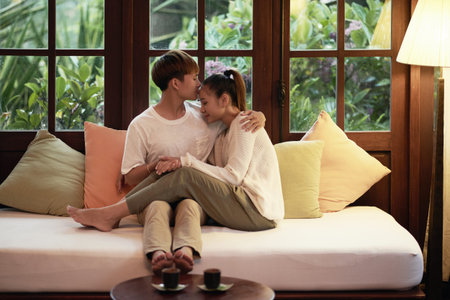 Young man sitting on sofa with his girlfriend and kissing herの写真素材