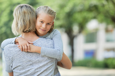 Pretty preteen woman hugging her mother and looking at cameraの写真素材