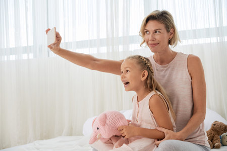 Cheerful mother and daughter taking selfie at home
