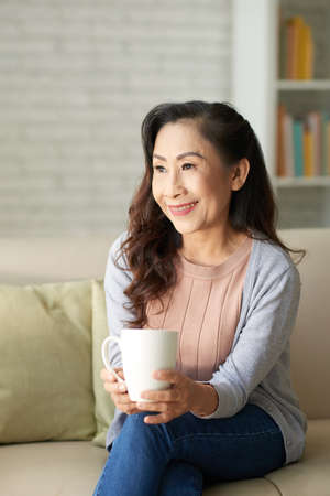 Happy elderly woman sitting with cup of coffee at homeの写真素材