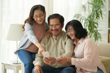 Senior man showing photos in his smartphone to two womenの写真素材