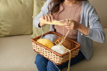 Woman sitting on sofa and knitting with yarnの写真素材