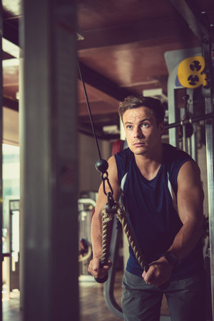 Handsome sporty man doing triceps exercise while having intensive training at spacious gym, portrait...