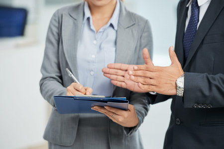 Close-up of businesswoman making notes in document with businessman standing near by her