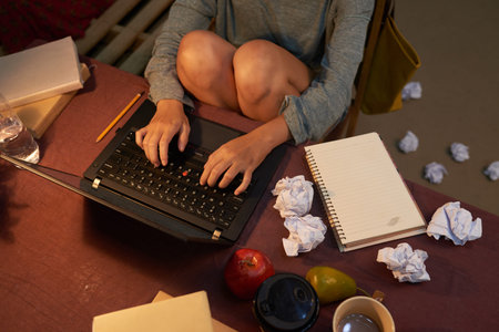 Creative woman working on laptop with crumpled drafts around