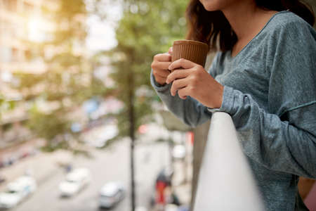 Cropped image of woman with cup of coffee standing on her balconyの写真素材