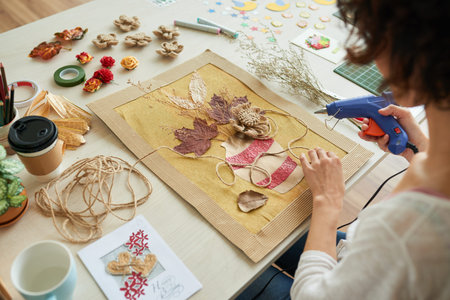 Close-up shot of creative designer using hot glue gun while sitting at studio desk and decorating...