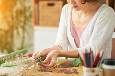 Creative woman wearing top and cardigan decorating bouquet of withered flowers with green ribbon while finishing decor item for living roomの写真素材