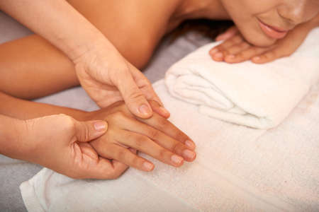 Spa salon master massaging hands of young woman over soft white towelの写真素材