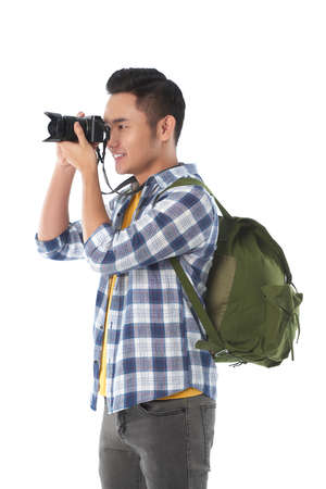 Profile view of handsome Asian tourist with backpack taking picture on modern camera, isolated on white backgroundの写真素材