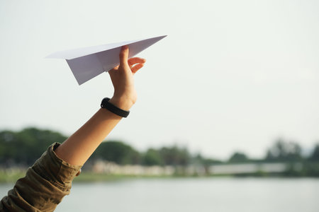 Close-up shot of female hand holding paper plane against sky, picturesque view on background