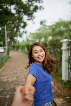 Beautiful Asian woman holding hand of crop anonymous beloved man asking to follow her while...