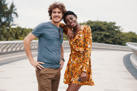 Beautiful and happy multiethnic couple in summer clothes standing and smiling at camera on...