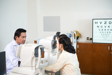 Focused Asian man in white gown using special machine and checking vision of mature woman during...