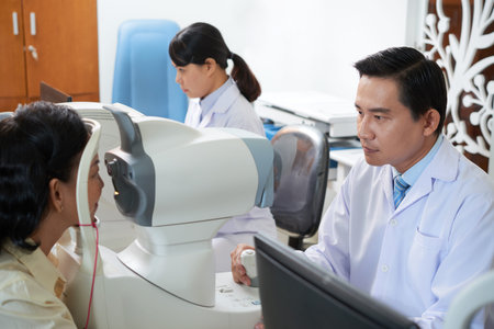 Concentrated Asian man checking vision of woman while working with colleague in cabinet of...