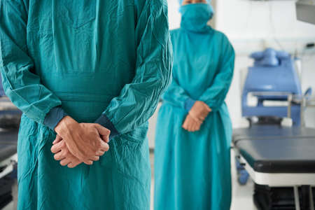 Faceless shot of professional surgeons in green sterile coats standing in operating room with hands togetherの写真素材