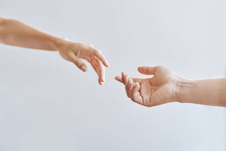 Crop hands of man and woman stretching towards to each other on grey backgroundの写真素材