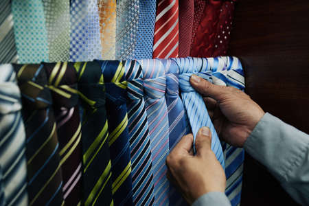 Hands of customer choosing perfect blue tie for his suitの写真素材