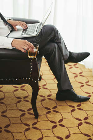 Stressed and tired businessman drinking rum and working on laptop during vacationの写真素材