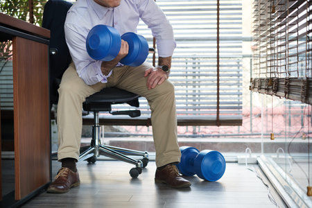 Businessman doing exercises with dumbbells during short break in officeの写真素材