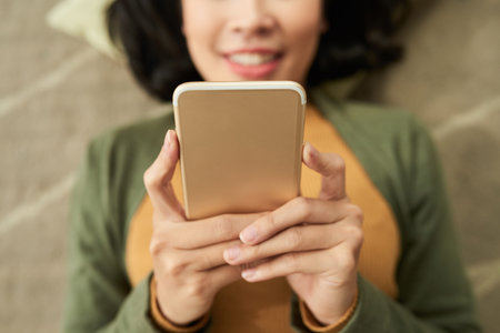 Close-up image of woman lying on floor and texting with friends