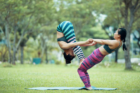 Side view of Asian female base bending back supporting flyer in forward fold standing on her hips in park on blurred backgroundの写真素材