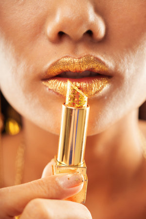 Crop close-up view of beautiful tanned female with slightly open mouth applying golden sparkling...