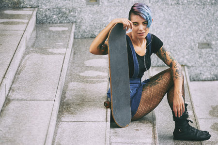 Young woman with colorful hair sitting on stairs with skateboard