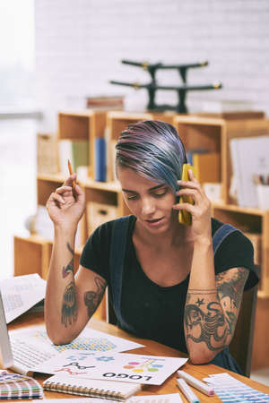 Creative female graphic designer discussing variant of company logotype with client on the phoneの写真素材