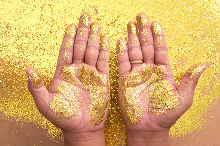 Crop shot from above of hands with palms covered in bright golden glitters above table with glitters