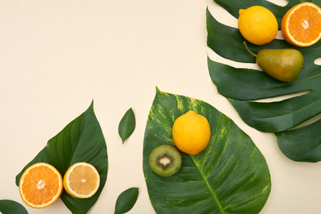 Top view of arranged ripe fruit mix with citrus and pear and kiwi on top of bright green Monstera...