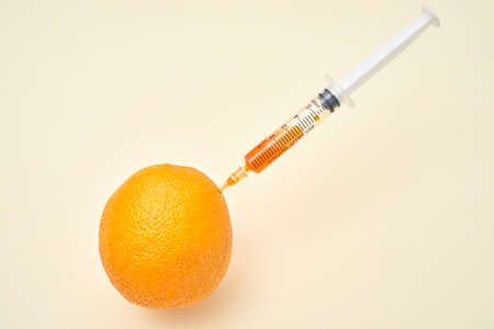 Bright ripe orange fruit with syringe extracting liquid and showing concept of cellulite treatment on white backgroundの写真素材