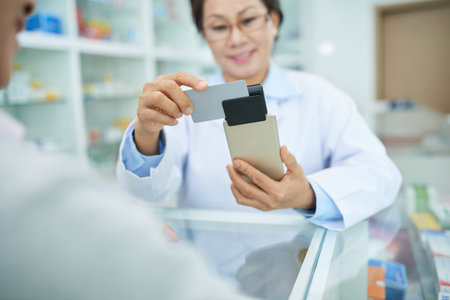 Smiling Vietnamese drugstore worker swiping credit card to accept payment