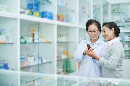 Cheerful Vietnamese pharmacist discussing medicine with senior female customerの写真素材