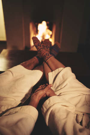 Couple in bath robes and warm socks resting by fireplaceの写真素材