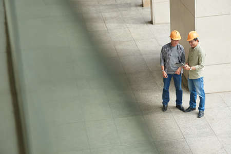 Smiling engineers in hard hats discussing information on digital tabletの写真素材
