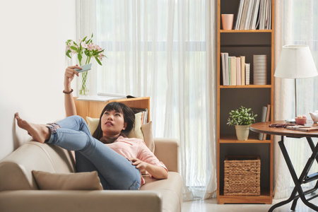 Attractive young Asian woman lying on sofa and talking selfies