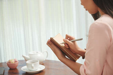 Woman drinking tea and writing plans and ideas in her diaryの写真素材