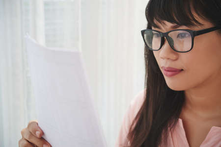 Smiling pretty young business woman in glasses reading documentの写真素材