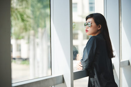 Beautiful fashionable young woman looking through office windowの写真素材