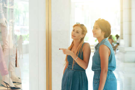 Young stylish girlfriends on street watching clothing in window case enjoying shopping lifestyle and leisureの写真素材