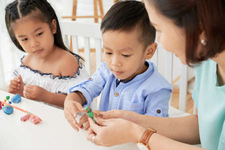 Teacher woman showing and helping with plasticine to cute Asian boy and girl in art classの写真素材