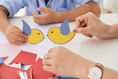Crop hands of teacher and boy playing with little birds cut-out of paper in art classの写真素材