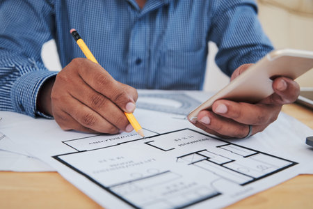 Unrecognizable Indian office worker sitting on desk and working on blue print while browsing...