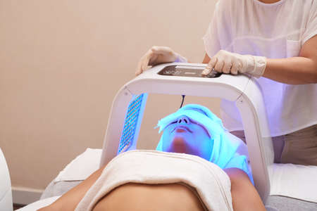Cosmetologist setting LED lamp for color light therapyの写真素材