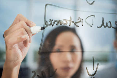 Asian female designer making notes on transparent board while presenting project in office