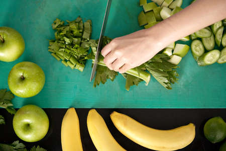 From above shot of crop hand chopping fresh celery while cooking in kitchenの写真素材