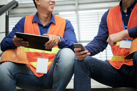 Crop men in waistcoats sitting on staircase and browsing digital devices during breakの写真素材