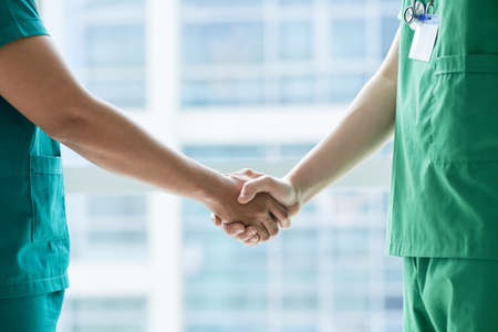 Side view of two men in scrubs standing near hospital window and shaking handsの写真素材